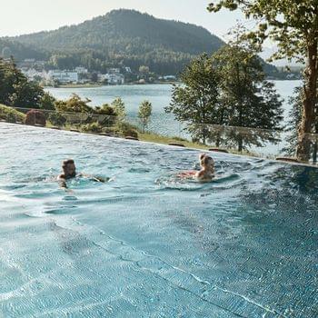 Piscina a sfioro Infinity Coppia che nuota in piscina a sfioro con vista su lago e montagne boscose